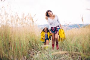 Mother with her cute daughter, walking through the meadow. Autumn, yellow grass. Caucasian, blond hair. Wearing rubber boots.
